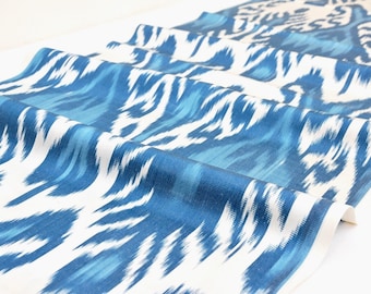 May include: White fabric with a blue ikat pattern. The fabric is folded and has a soft, flowing texture.