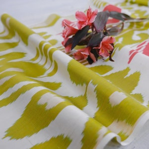 May include: White fabric with a green and white ikat pattern. The fabric is folded and draped with a bouquet of pink flowers.