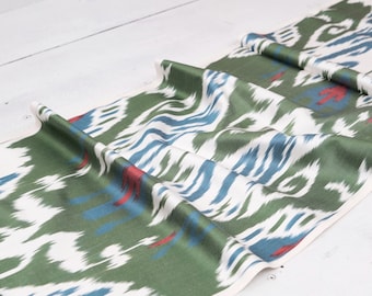 May include: Green, white, and blue ikat fabric with a subtle red pattern. The fabric is folded and draped on a white surface.