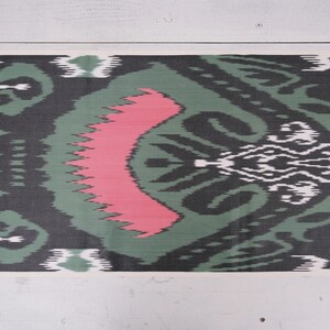 May include: A close-up of a green and black fabric with a pink and white pattern. The fabric has a traditional ikat design.