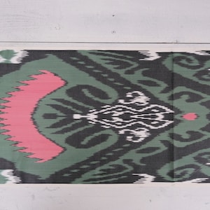 May include: A green, black, and pink patterned fabric with a traditional ikat design. The fabric has a white background with a repeating pattern of swirls and diamonds.