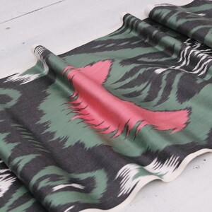 May include: Green, black, and pink patterned fabric with a white border. The fabric has a wavy, flowing design.