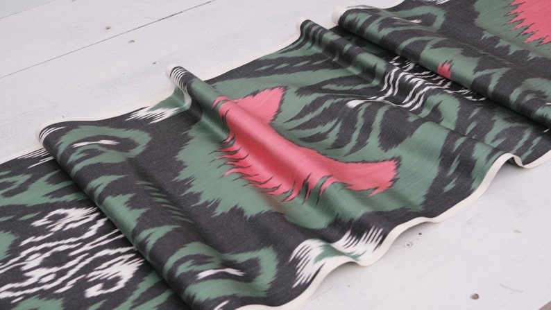 May include: Green, black, and pink patterned fabric with a white border. The fabric has a wavy, flowing design.