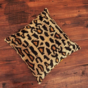 May include: A square cushion with a leopard print pattern in shades of black, gold, and brown. The cushion is made of a soft, plush fabric.