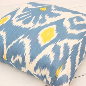May include: A blue and white patterned throw pillow with yellow accents. The pillow is made of a soft, woven fabric and has a square shape.