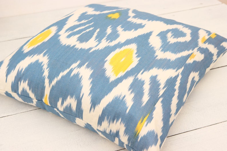 May include: A blue and white patterned throw pillow with yellow accents. The pillow is made of a soft, woven fabric and has a square shape.