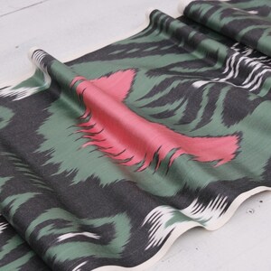 May include: Green, black, and pink patterned fabric with a white border. The fabric is folded and has a wavy edge.
