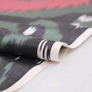 May include: Close-up of a folded fabric with a black, green, and white abstract pattern. The fabric has a white border with black stripes.