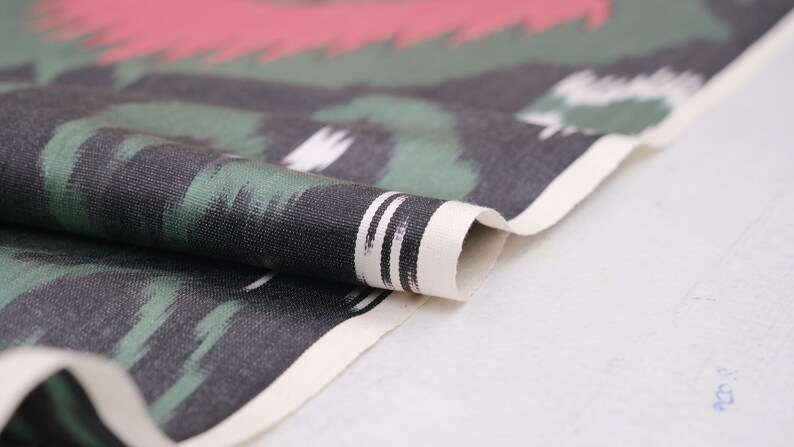 May include: Close-up of a folded fabric with a black, green, and white abstract pattern. The fabric has a white border with black stripes.