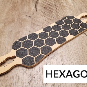 Może przedstawiać: Drewniany deck do longboarda z czarnym, sześciokątnym wzorem taśmy antypoślizgowej. Deck jest jasnobrązowy i ma wycięcie na trucki. Tekst "HEXAGON" jest nadrukowany czarnym kolorem na białym tle pod deską.