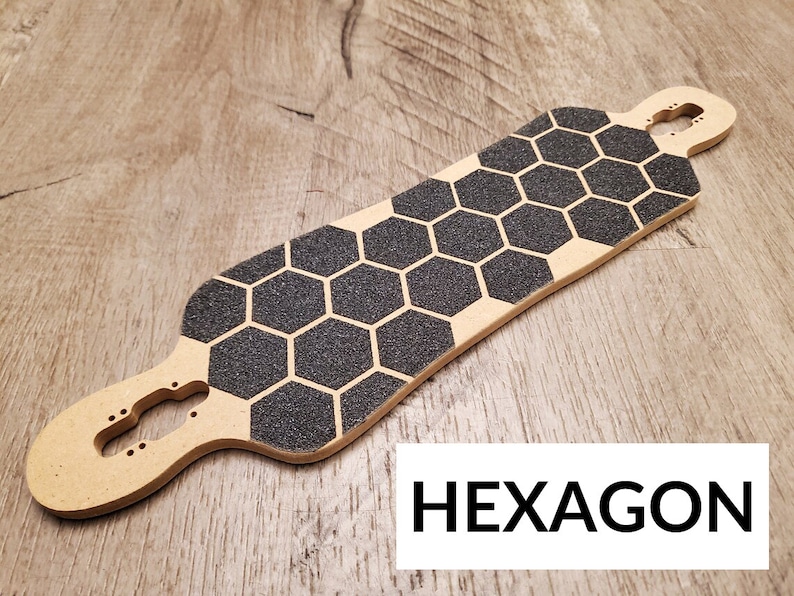 Może przedstawiać: Drewniany deck do longboarda z czarnym, sześciokątnym wzorem taśmy antypoślizgowej. Deck jest jasnobrązowy i ma wycięcie na trucki. Tekst "HEXAGON" jest nadrukowany czarnym kolorem na białym tle pod deską.