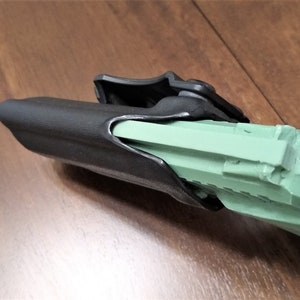 May include: A black polymer holster with a green plastic gun inside. The holster has a clip on the back for attaching to a belt.