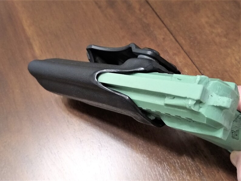 May include: A black polymer holster with a green plastic gun inside. The holster has a clip on the back for attaching to a belt.