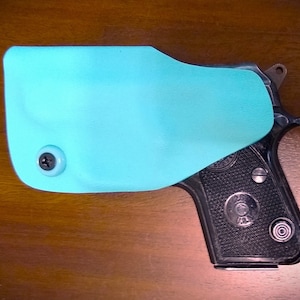 May include: A light blue leather holster with a screw on the side, covering a black handgun with a textured grip and a silver barrel.