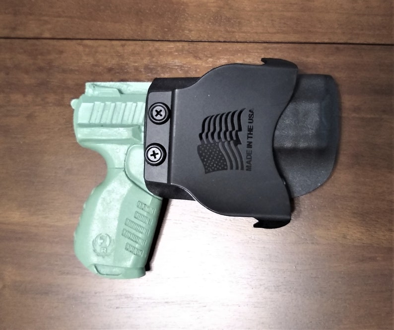May include: A green handgun with a black holster. The holster has the text "Made in the USA" and an American flag design.