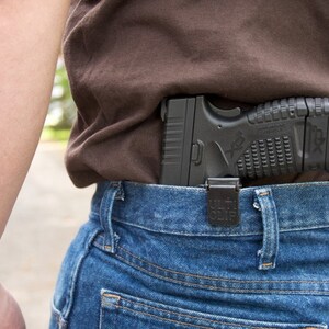 May include: A black handgun is tucked into the waistband of a pair of blue jeans. The gun is secured with a black holster. The person wearing the jeans has a tattoo on their arm that reads "But Fear Is a Choice."