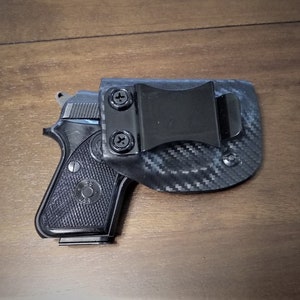 May include: A black handgun with a black carbon fiber holster. The holster has a metal clip for attaching to a belt.