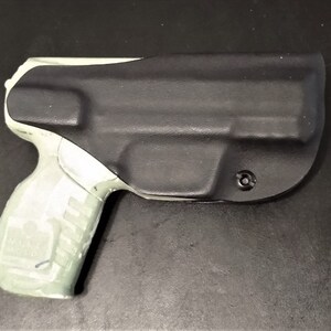 May include: A black and gray gun holster with a light gray handgun inside. The holster is made of a textured material and has a small hole on the side.