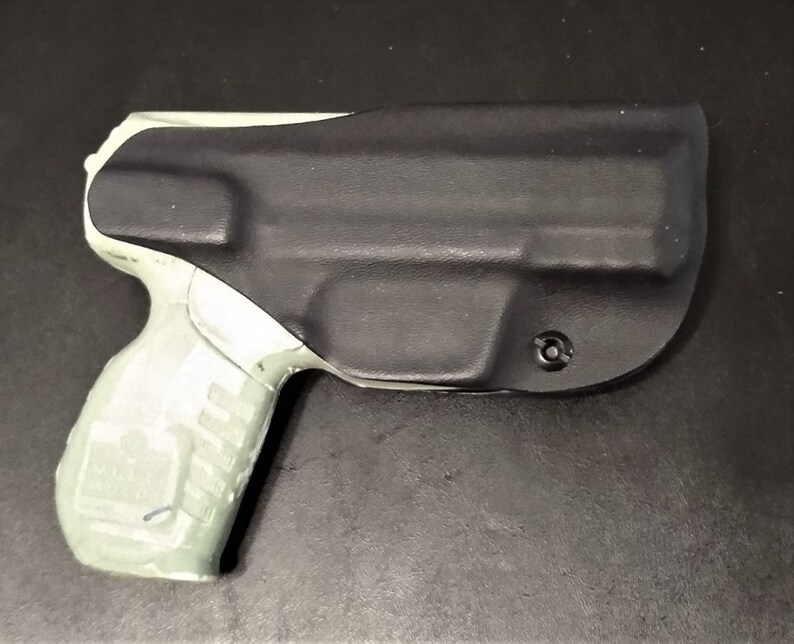 May include: A black and gray gun holster with a light gray handgun inside. The holster is made of a textured material and has a small hole on the side.