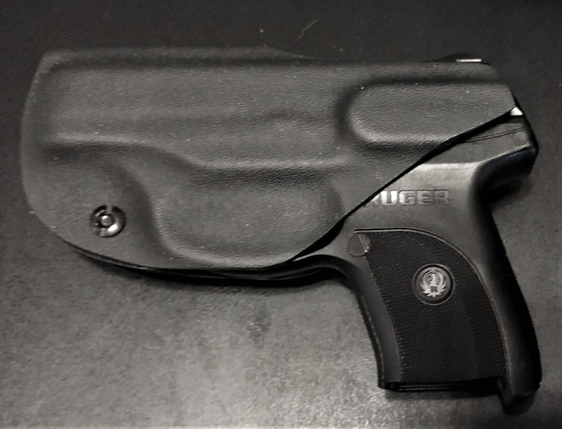 Puede incluir: Una pistola negra con una funda negra. La pistola tiene un logotipo Ruger plateado en el lateral.