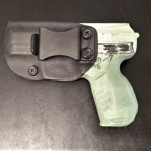 May include: A black polymer holster with a clip for a handgun. The holster is designed to fit a semi-automatic pistol with a black polymer frame and a silver slide. The gun is partially visible in the holster.