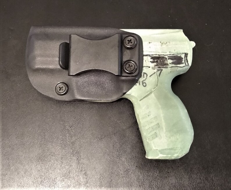 May include: A black polymer holster with a clip for a handgun. The holster is designed to fit a semi-automatic pistol with a black polymer frame and a silver slide. The gun is partially visible in the holster.