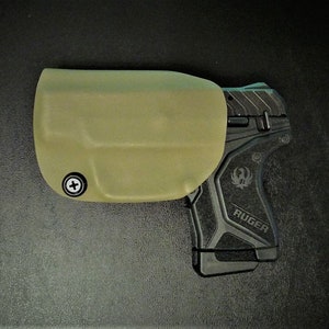 May include: A tan leather holster with a black Ruger pistol inside. The holster has a screw on the side.
