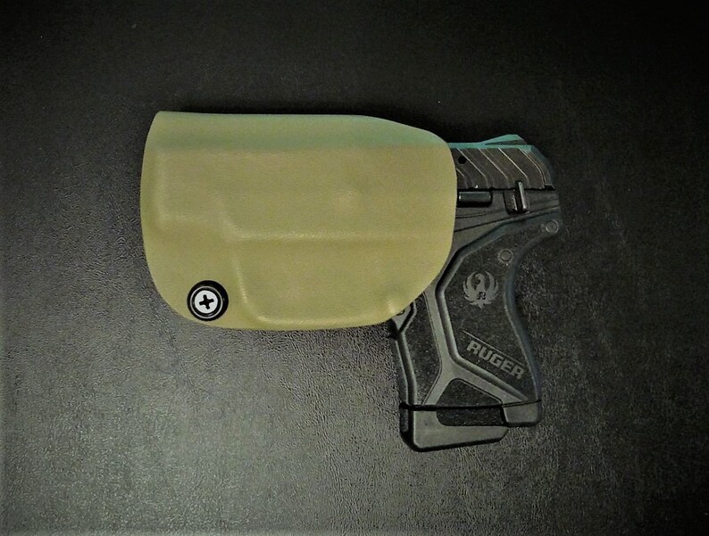 May include: A tan leather holster with a black Ruger pistol inside. The holster has a screw on the side.