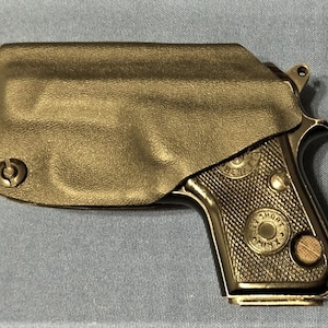 May include: A black leather holster with a small, black handgun inside. The holster has a snap closure and a small metal loop on the side. The handgun has a black grip and a silver barrel.