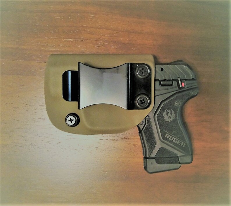 May include: A tan leather holster with a black metal clip and a black Ruger pistol with a textured grip.