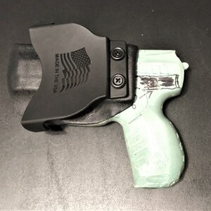May include: A black leather holster with a  'MADE IN THE USA' inscription and an American flag design. The holster is holding a light green handgun.