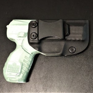 May include: A black and green handgun in a black holster with a clip. The holster has a screw on the side.