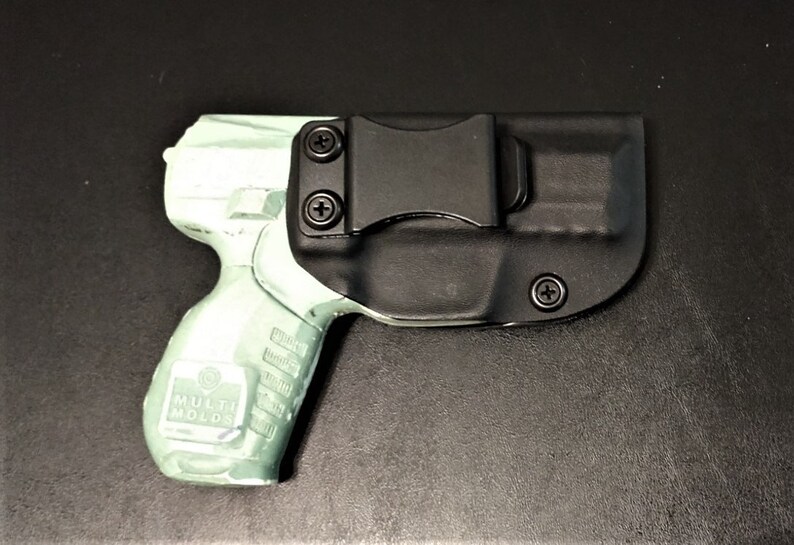 May include: A black and green handgun in a black holster with a clip. The holster has a screw on the side.