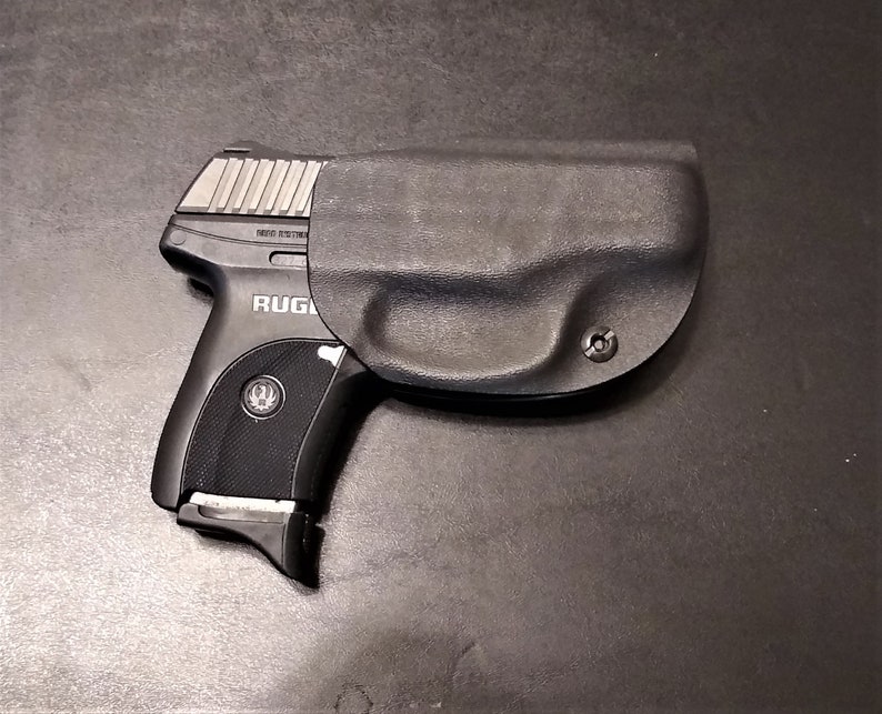 Puede incluir: Una pistola negra con una funda negra. La pistola tiene un deslizador plateado y el texto "RUGER" es visible en el lateral.