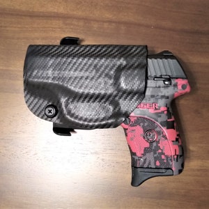 Puede incluir: Una pistola con estampado negro y rojo con una funda de fibra de carbono negra. La funda tiene un tornillo en el lateral.