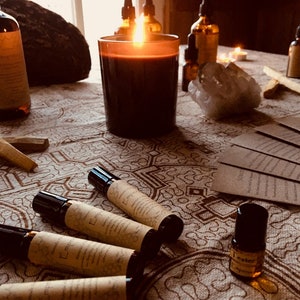 May include: A table setting with a lit candle, several small bottles of essential oils, and a few roller bottles labeled "Empress" and "Icestor Empress". The table has a patterned tablecloth.