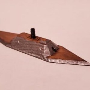 May include: A small, gray and brown model of a Civil War era ironclad warship. The model has a raised deck and a single smokestack.