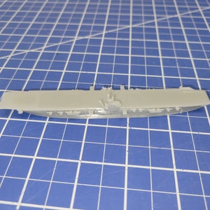 Puede incluir: Un modelo de portaaviones de plástico blanco. El modelo está detallado con una cubierta de vuelo, una isla y aviones.