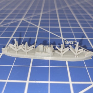 Puede incluir: Un modelo de barco de carga de plástico gris con múltiples mástiles y una cubierta elevada. El barco está sentado sobre una superficie azul cuadriculada.