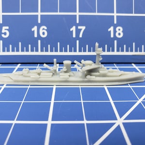 Puede incluir: Un modelo de barco de guerra de plástico gris con un diseño detallado. El modelo mide aproximadamente 15 cm de largo y tiene una cubierta elevada con múltiples torretas de cañones y otros detalles.