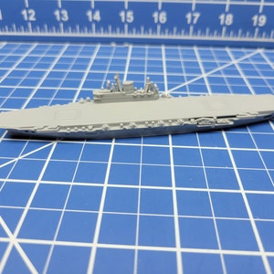 Puede incluir: Un modelo de plástico gris de un portaaviones con una cubierta plana y una superestructura elevada. El modelo está sentado sobre una superficie azul enrejada.