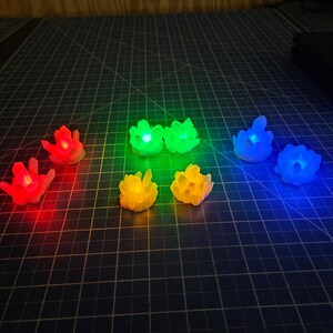 May include: A collection of seven glowing, colorful crystal-shaped LED lights. The lights are arranged on a dark surface, with each emitting a different color: red, green, yellow, and blue. The crystals are approximately 2 inches in height.