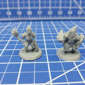 May include: Two grey plastic miniature figures of fantasy creatures with flame-like hair. The figures are standing on round bases.