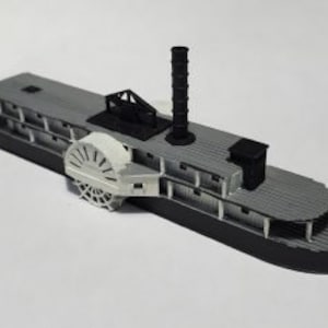 May include: A gray and black model of a steamboat with a white paddle wheel. The model is detailed with a smokestack and a railing.
