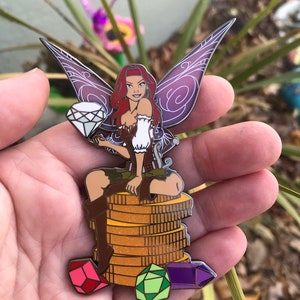 May include: A colorful enamel pin featuring a fairy with red hair, purple wings, and a diamond. The fairy is seated on a stack of gold coins, with colorful gems at the base. The pin is a collectible item.