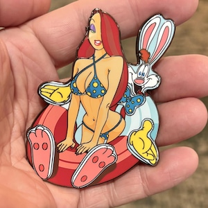 Puede incluir: Un colorido pin de esmalte con un personaje de dibujos animados en un bikini azul con lunares, sentado con un conejo blanco. El pin tiene detalles en rojo, amarillo y azul, con un acabado brillante.