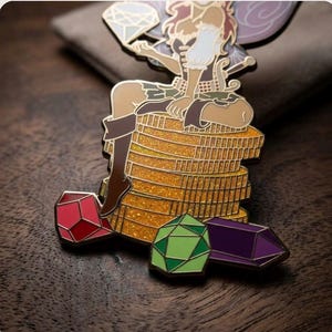 May include: A detailed enamel pin featuring a fairy sitting atop a stack of gold coins. The fairy holds a diamond and is surrounded by red, green, and purple gemstone pins. The pin has a glittery gold background and is set against a dark wood surface.