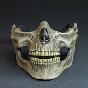Pu&ograve; includere: Una maschera a teschio dettagliata, a mezza faccia, con finitura color osso invecchiata. La maschera presenta dettagli realistici dei denti e della cavit&agrave; nasale, con un cinturino nero per fissarla. Progettata per costumi o decorazioni.