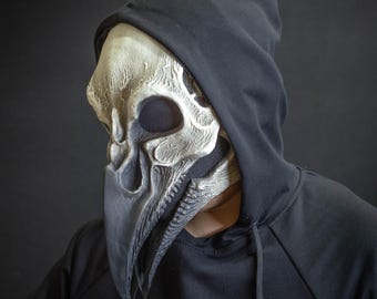 Op de afbeelding: Een persoon draagt ​​een zwarte hoodie met een wit en grijs schedelmasker met een lange snavel.