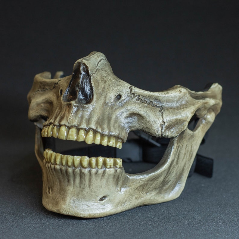 Pu&ograve; includere: Una maschera a teschio dettagliata, a mezza faccia, con finitura invecchiata color osso. La maschera presenta denti realistici e dettagli intricati della struttura ossea. Cinghie nere visibili per fissare la maschera. Tema Halloween o cosplay.